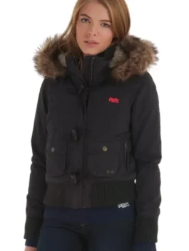 A young woman posing in a short, black Superdry Study Duffle Jacket. The jacket is a puffer style with a ribbed waistband and cuffs, large front flap pockets with toggle closures, and a hood trimmed with thick brown Vegan fur. The red embroidered Superdry logo is visible on the chest.
