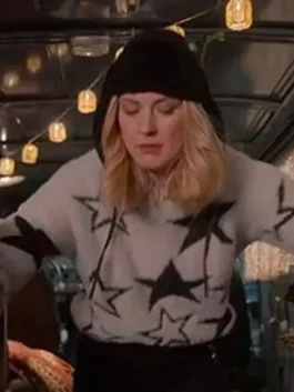 Blonde woman wearing a white star sweater and black beanie in a festive outdoor setting with string lights.