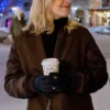 A medium shot of Alexandra Breckenridge standing outside in the snow, wearing a brown coat and black gloves, holding a holiday-themed coffee cup.