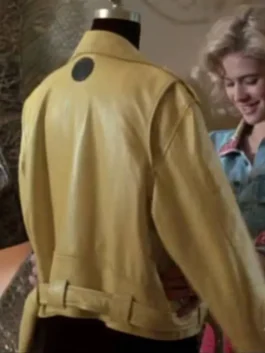 Back view of the yellow leather jacket displaying a distinctive black circular patch on the upper back, with actress Kristy Swanson visible in the background.