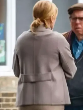 Back view of a woman wearing a light grey belted coat with a center seam, standing outdoors and talking to a man.