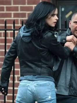 Back/side view of Jessica Jones (Krysten Ritter) in her cropped black leather jacket and distressed jeans, engaging in a physical confrontation on a city street.