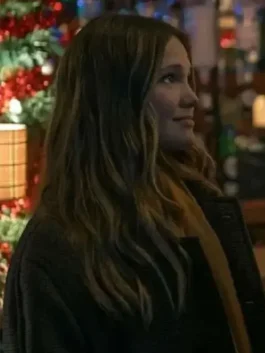 Olivia Holt Jingle Bell Heist brown coat. Side profile of Sophia (Olivia Holt) with wavy hair, wearing the Brown Long Coat near a festive, lit holiday display.