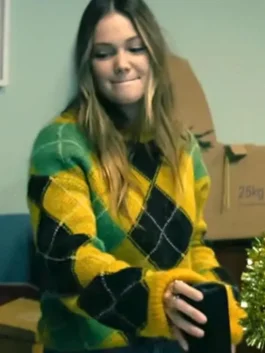 Olivia Holt wearing a yellow fuzzy argyle sweater while seated indoors.