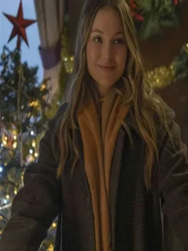 Olivia Holt Jingle Bell Heist long coat in a close-up shot. Sophia wears the Brown Long Coat and a scarf, smiling with Christmas lights behind her.