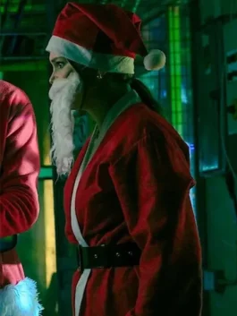 A woman in a red Santa costume with a white beard and hat stands in a dimly lit, festive indoor setting.