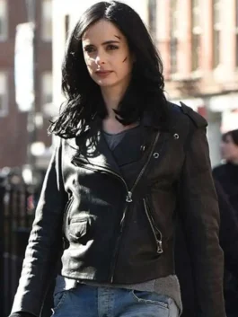 Krysten Ritter as Jessica Jones in a medium shot, wearing her asymmetrical black leather jacket and looking serious, with marks visible on her face.