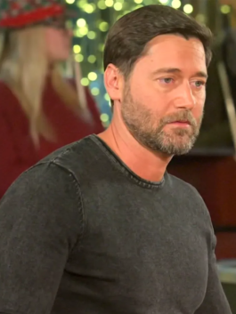 Man wearing a dark charcoal plain knitted pullover in an indoor holiday setting with blurred lights.