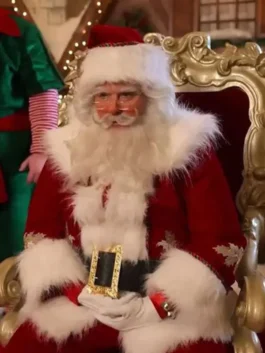 Santa Claus sitting on an ornate chair in a red coat with white fur trim, wearing glasses and white gloves, with holiday decor behind him.