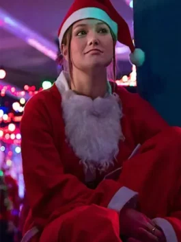 Olivia Holt in a red Santa coat and hat sits with her arms crossed in a brightly lit festive space.