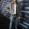 A full-length view of The Housemaid Brandon Sklenar grey jacket. This Andrew Winchester grey wool jacket is styled with blue jeans and boots.