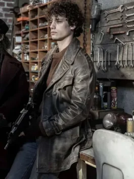 Character Emile from The Walking Dead in a distressed, double-breasted leather coat and sweater, holding a rifle in a cluttered workshop.