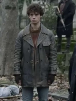 Full body shot of Emile standing in a bleak outdoor setting, wearing the distressed, mid-length, double-breasted leather coat and fingerless gloves.