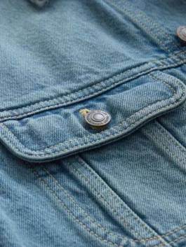 Close-up of a high-quality blue denim jacket for men & women featuring a durable metal button and detailed stitching on the front pocket flap.