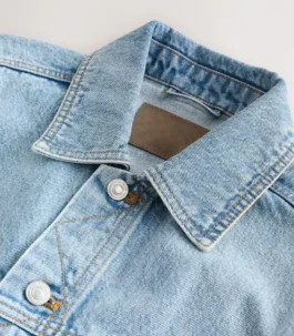 Detailed view of the collar and buttons on a Light Blue jeans Blue jacket. A stylish Light Blue denim style jacket featuring classic orange stitching.
