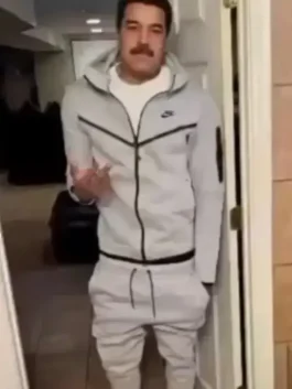 A full-body shot of a man with a mustache who resembles Nicolás Maduro, wearing a light grey Tech Fleece tracksuit. He is standing in a doorway indoors, gesturing with one hand.