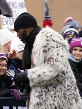 Randy Moss interacting with fans while wearing his signature Randy Moss NFL fur coat and a black beanie during a winter football broadcast.