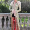 Margot Robbie wearing a John Galliano long trim coat in vintage floral brocade with pink feathered trim on a red carpet.