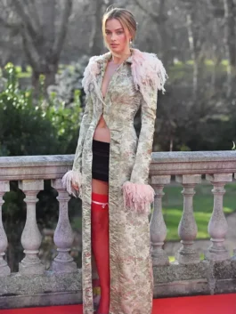 Margot Robbie John Galliano long trim coat during the Wuthering Heights London photocall, styled with a black mini skirt and red hosiery.