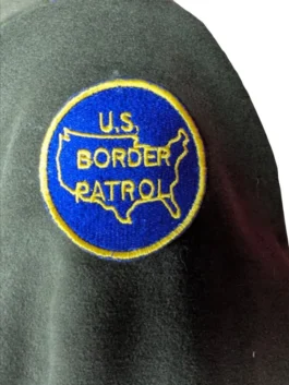 Embroidered blue and yellow U.S. Customs and Border Protection Department of Homeland Security shield patch on a dark green fabric surface.
