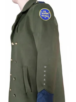 Side profile view of a dark green double-breasted trench coat on a mannequin highlighting the circular U.S. Border Patrol patch and five embroidered stars on the sleeve.
