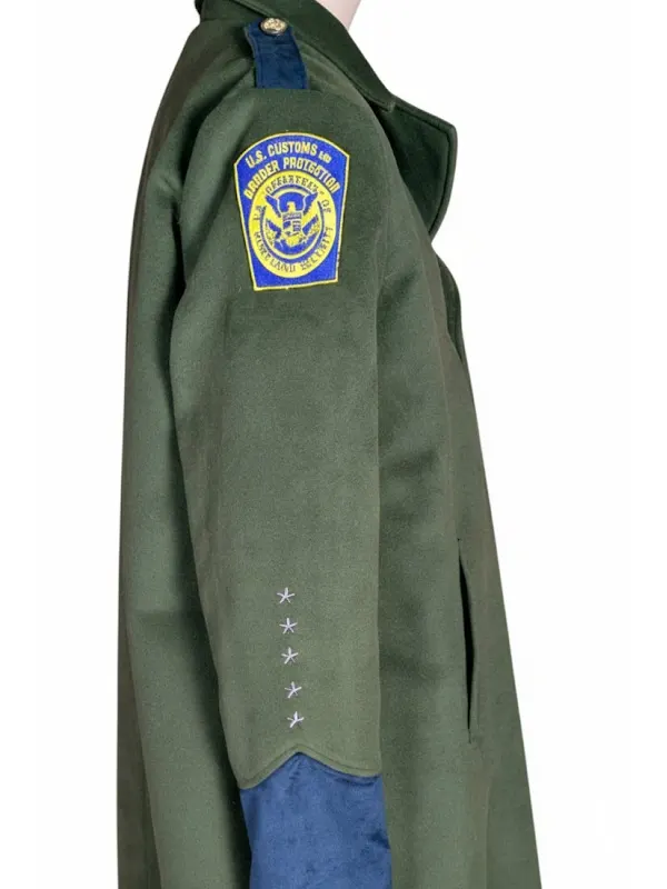 Right profile view of a dark green uniform trench coat on a mannequin featuring the shield-shaped U.S. Customs and Border Protection insignia and star embroidered sleeve detailing.