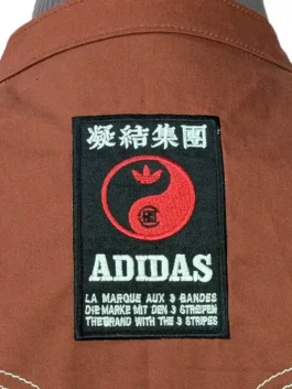 Close-up of the rectangular woven collaboration patch on the back of the brown Adidas CLOT Chinese New Year track jacket.