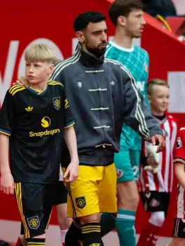 Manchester United player in grey Adidas CNY jacket walking with mascot during Premier League Matchday 36 at Sunderland Stadium