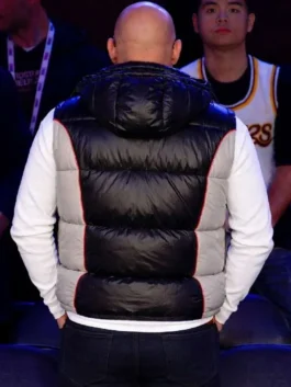 Rear view of Vin Diesel showing the back of a black and grey puffer hooded vest with red piping details, layered over a white long-sleeve shirt.