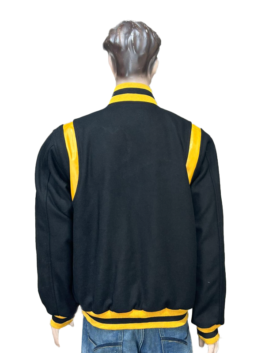 Rear view of a black wool varsity jacket on a mannequin, featuring gold leather shoulder inserts and a gold and black striped rib-knit collar, cuffs, and hem.