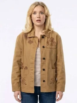 Full front view of Amalia Williamson wearing the brown cotton utility jacket from You're Killing Me S01, featuring dark button closures, large patch pockets, and dark brown floral embroidery on the chest and lower pockets.