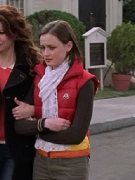 Full-length view of Alexis Bledel as Rory Gilmore wearing a red, orange, and yellow puffer vest paired with a scarf and trousers.