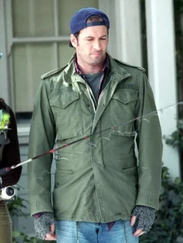 Front view of Luke Danes holding a fishing rod, dressed in a green cotton utility jacket with shoulder epaulets, a backward blue cap, and grey fingerless gloves.