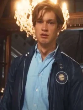 Front view of James Beaufort played by Damian Hardung wearing an open blue bomber jacket with a circular crest patch over a light blue shirt.