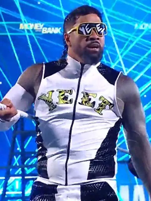 Medium shot of Jey Uso looking ahead, wearing yellow-rimmed "YEET" sunglasses and a white and black zippered vest with "YEET" printed in a yellow-and-black pattern across the chest.