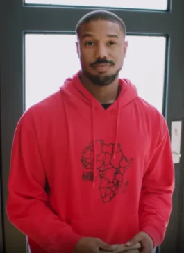 Michael B. Jordan wearing a vibrant red pullover hoodie featuring a black outline map graphic of Africa printed on the front.