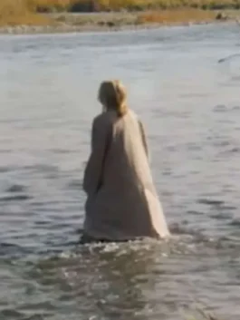 Back view of Michelle Pfeiffer in The Madison wearing a long beige wool trench coat while walking in shallow water.