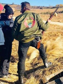Rear view of Sylvester Stallone on set wearing the olive green satin bomber jacket with a large red wings and skull graphic on the back.