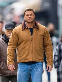 Alan Ritchson walking on a city street as Jack Reacher in Season 2 wearing a brown canvas cotton jacket with a corduroy collar.