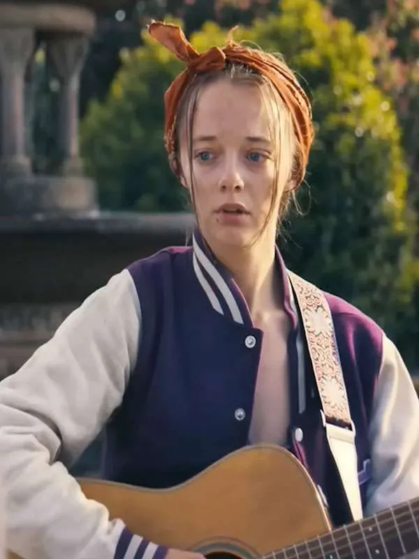 Front view of Ellie de Lange wearing a purple and white varsity bomber jacket with silver snap-button closures while playing an acoustic guitar.