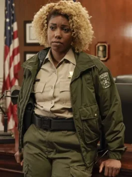 Sheriff Josie Miller wearing an olive green tactical zip-up jacket with a shoulder patch, stand-up collar, and cargo front pockets in Will Trent.