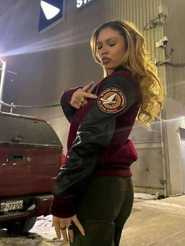 A woman posing from the side to show off the maroon Starfleet Academy varsity bomber jacket with black leather sleeves and a round sleeve patch.