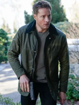 Justin Hartley as Colter Shaw holding a firearm while wearing the Tracker Season 2 olive green jacket over a grey t-shirt.