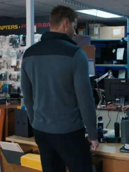 Back view of Justin Hartley as Colter Shaw in Tracker S02 wearing a grey and black puffer jacket indoors.