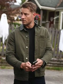 Justin Hartley holding a smartphone outdoors, wearing the Tracker Season 3 Colter Shaw green cotton jacket with a chest pocket.