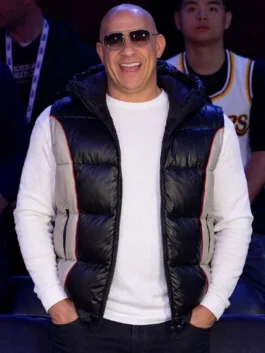 Front view of Vin Diesel standing with hands in his pockets, wearing his black and grey 75th All-Star Game hooded puffer vest and sunglasses.
