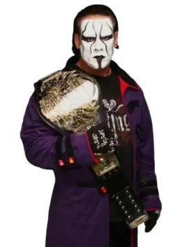 Frontal medium shot of WWE wrestler Sting holding a gold championship belt over his shoulder while wearing a purple coat and his iconic black and white face paint.