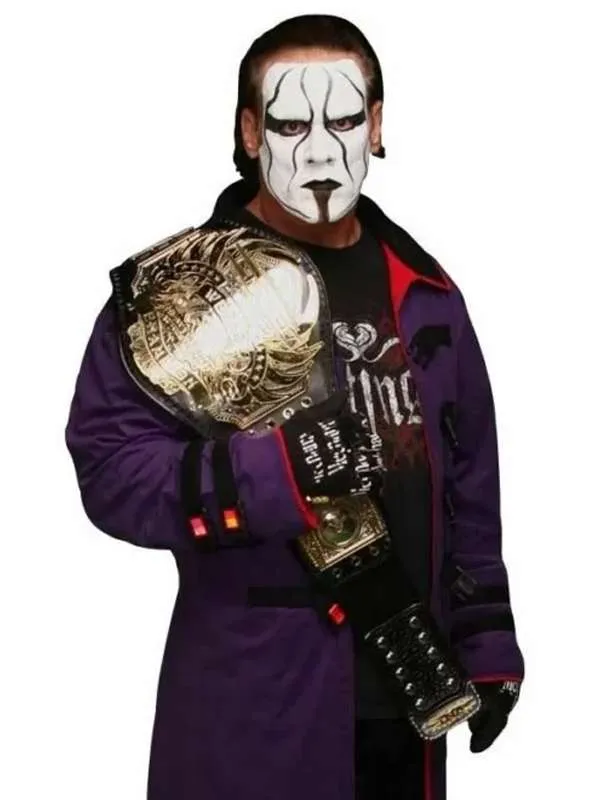 Frontal medium shot of WWE wrestler Sting holding a gold championship belt over his shoulder while wearing a purple coat and his iconic black and white face paint.