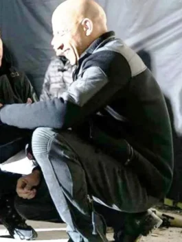 Side profile of Vin Diesel crouching on set, wearing a black and grey sporty hybrid jacket with matching athletic pants.